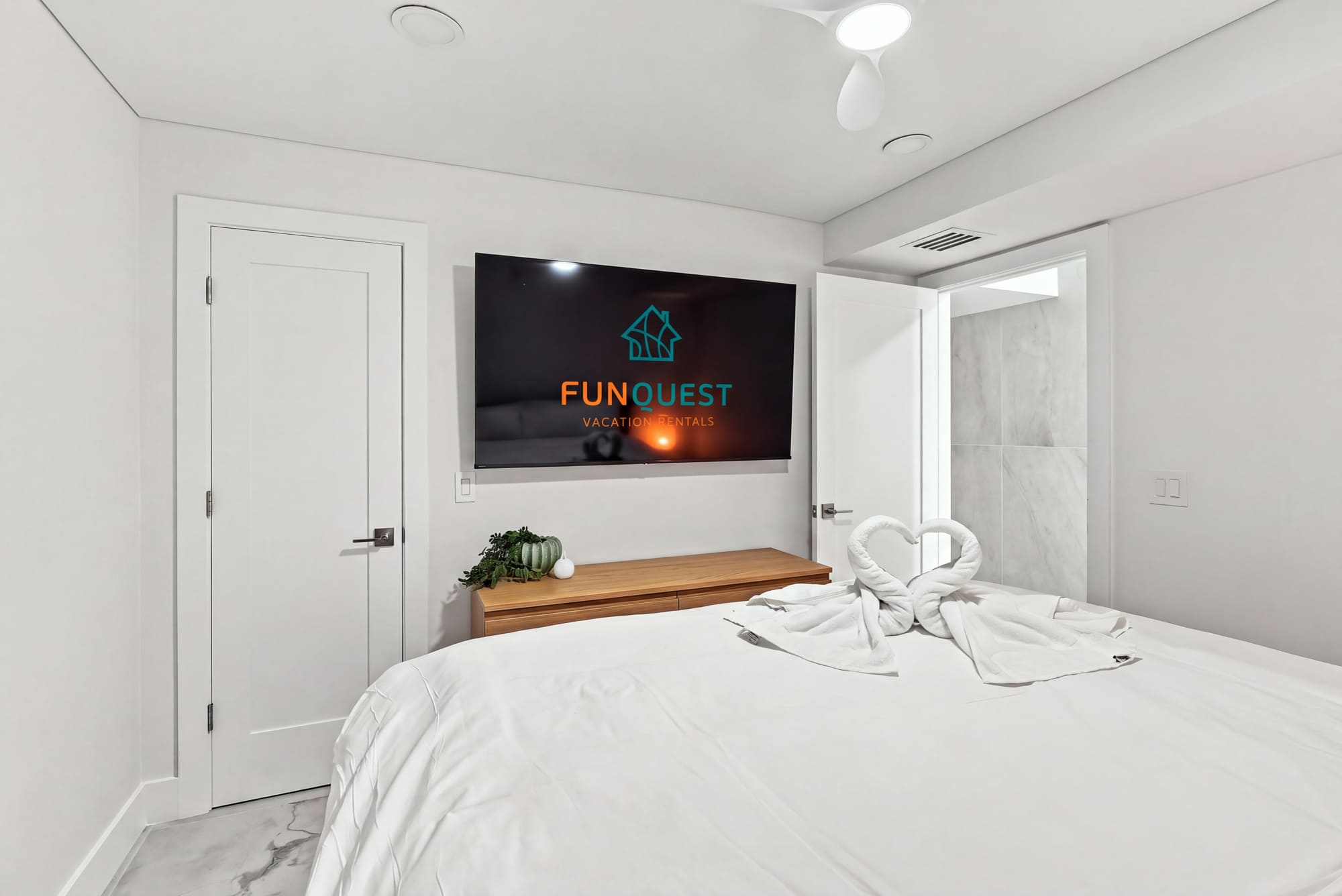 The Summit 1512 – Modern bedroom with a large TV, wooden dresser, and towel swans on the bed.