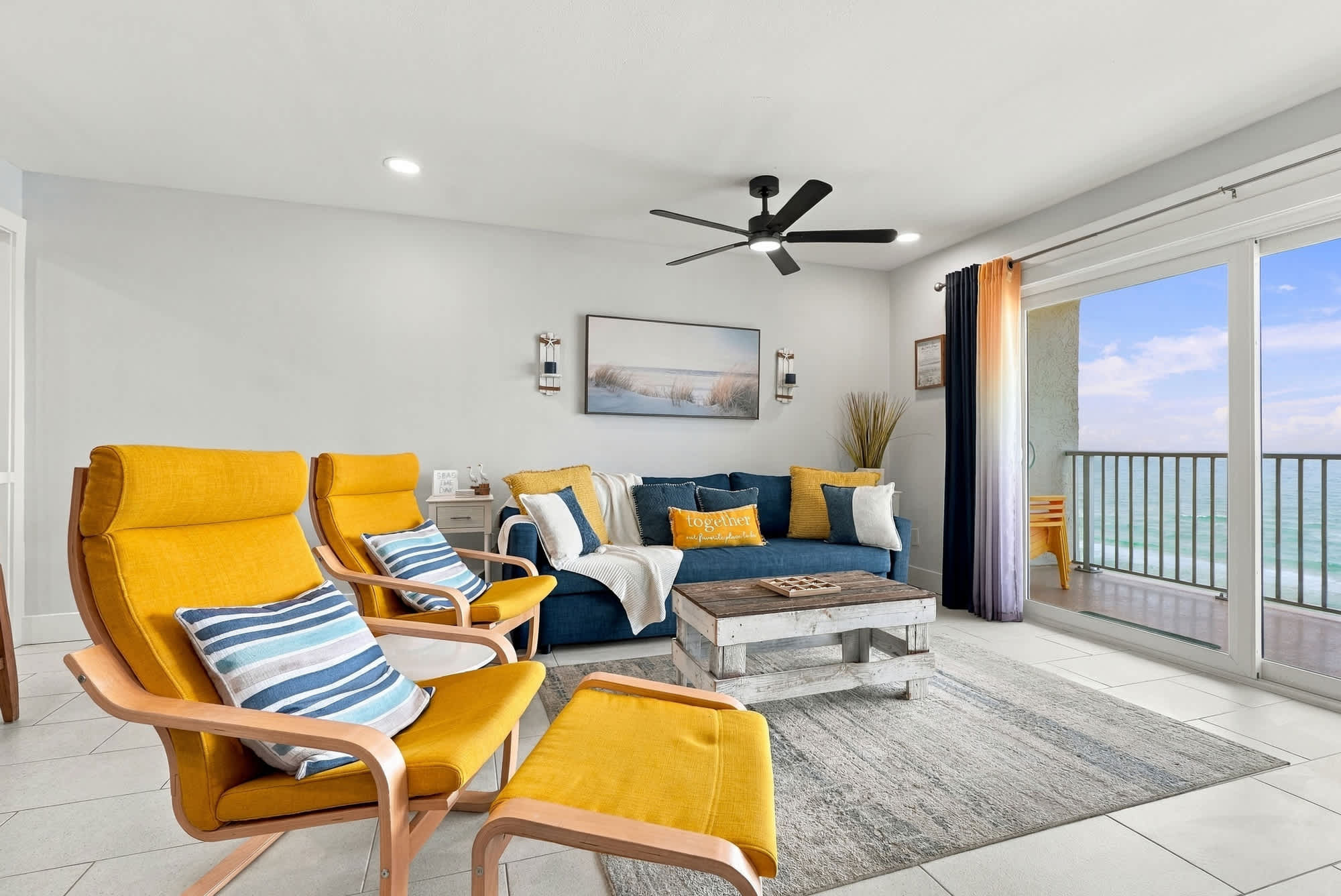 The Summit 1122  – Bright living room with two yellow chairs, a blue sofa, ocean view, and sliding glass doors.