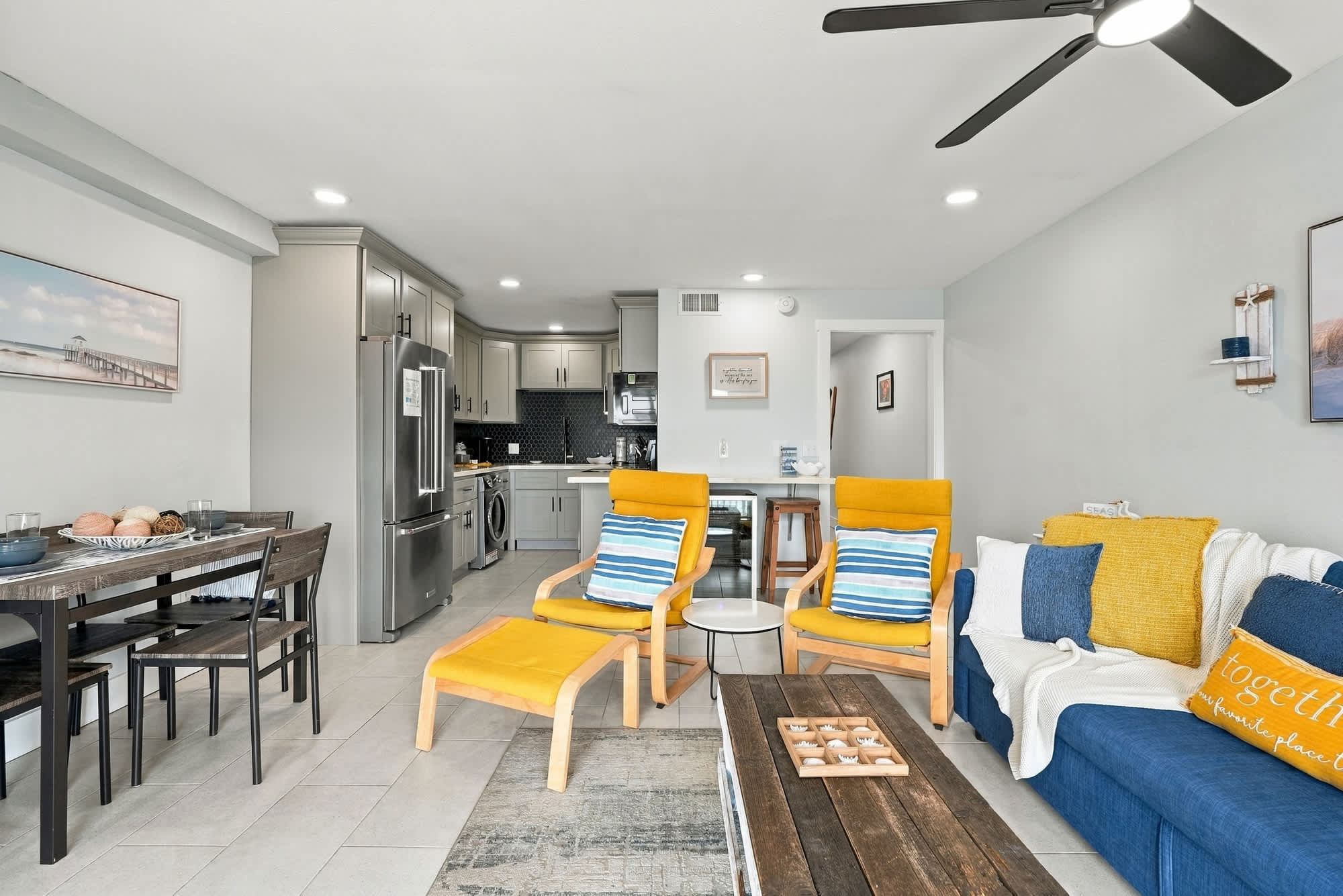 The Summit 1122  – Living room with two yellow chairs, a blue sofa, dining table, and kitchen in background.