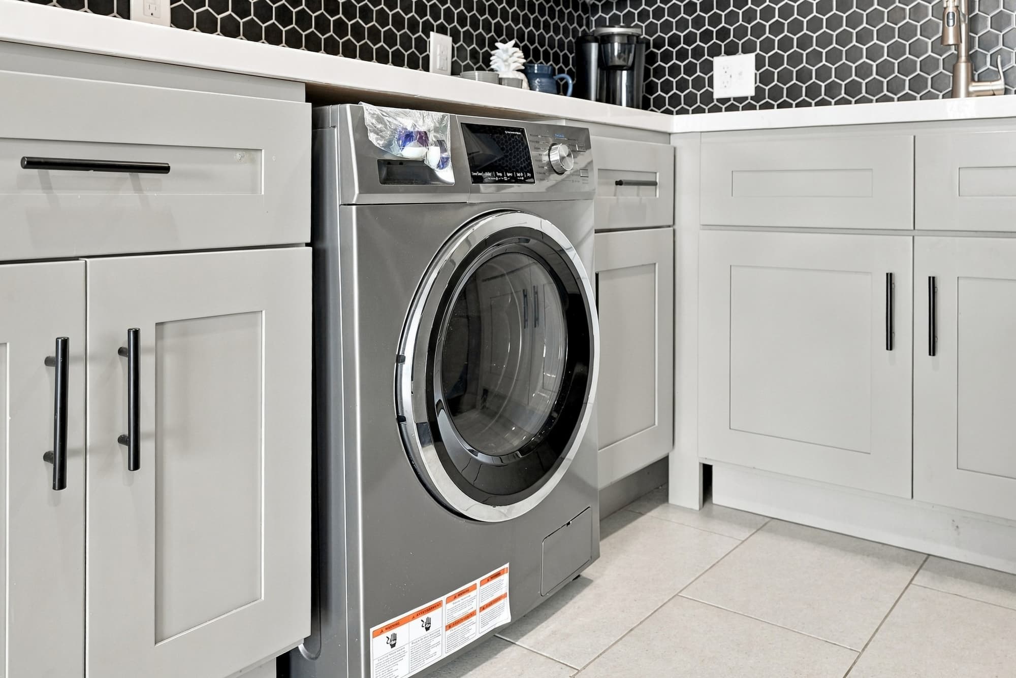 The Summit 1122  – Washer and dryer integrated into kitchen cabinetry with gray finishes and hexagonal black tile backsplash.