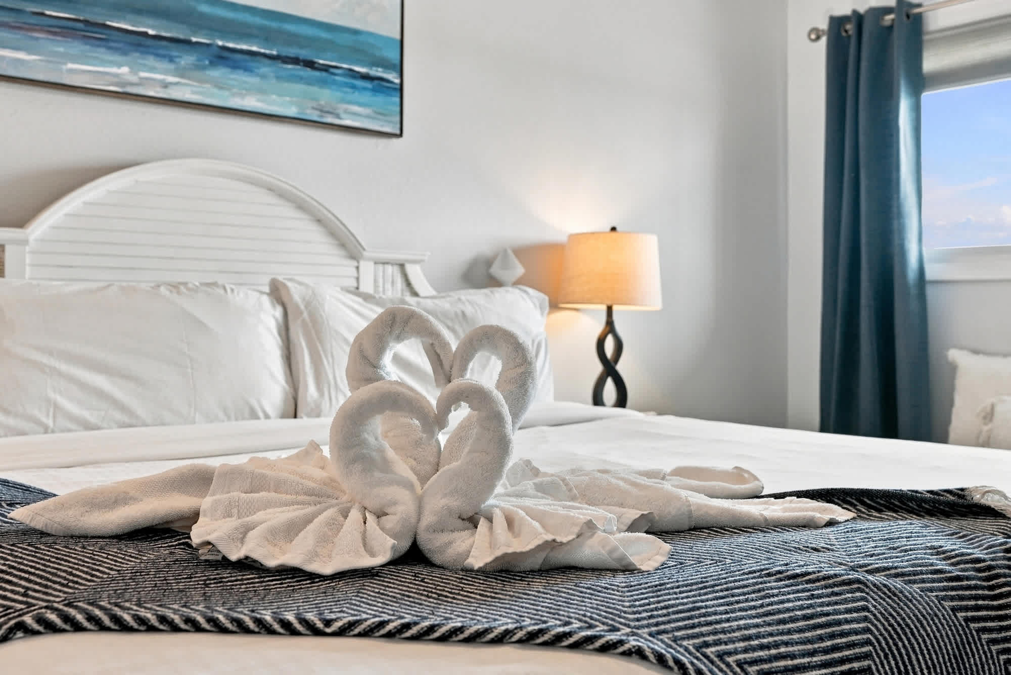 The Summit 1122  – Cozy bedroom with a white bed, decorative towel swans, and a lamp beside a window.