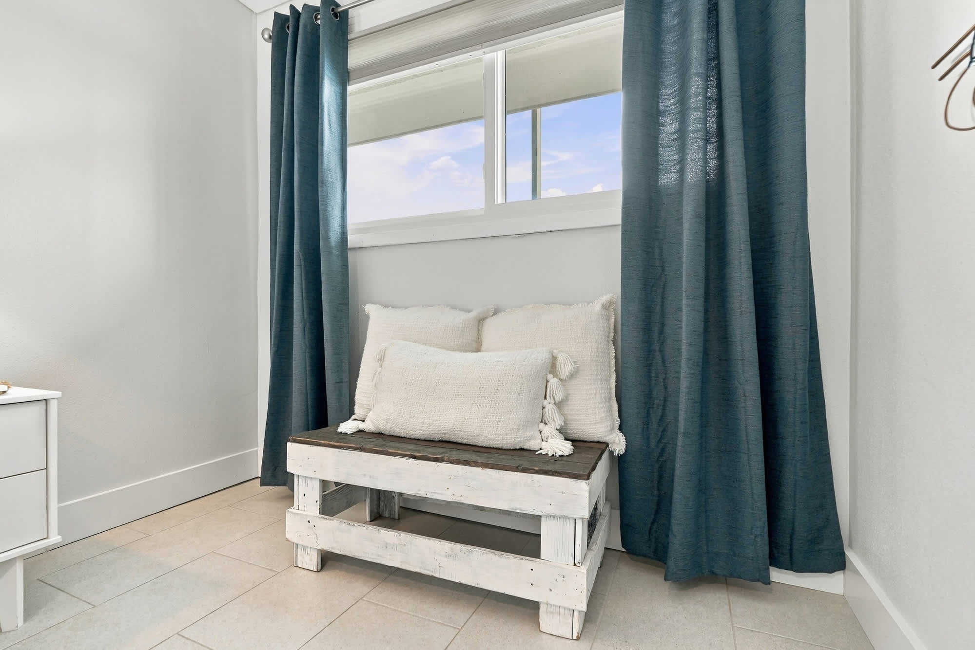 The Summit 1122  – Cozy seating area with a wooden bench, cushions, and blue curtains by a window.