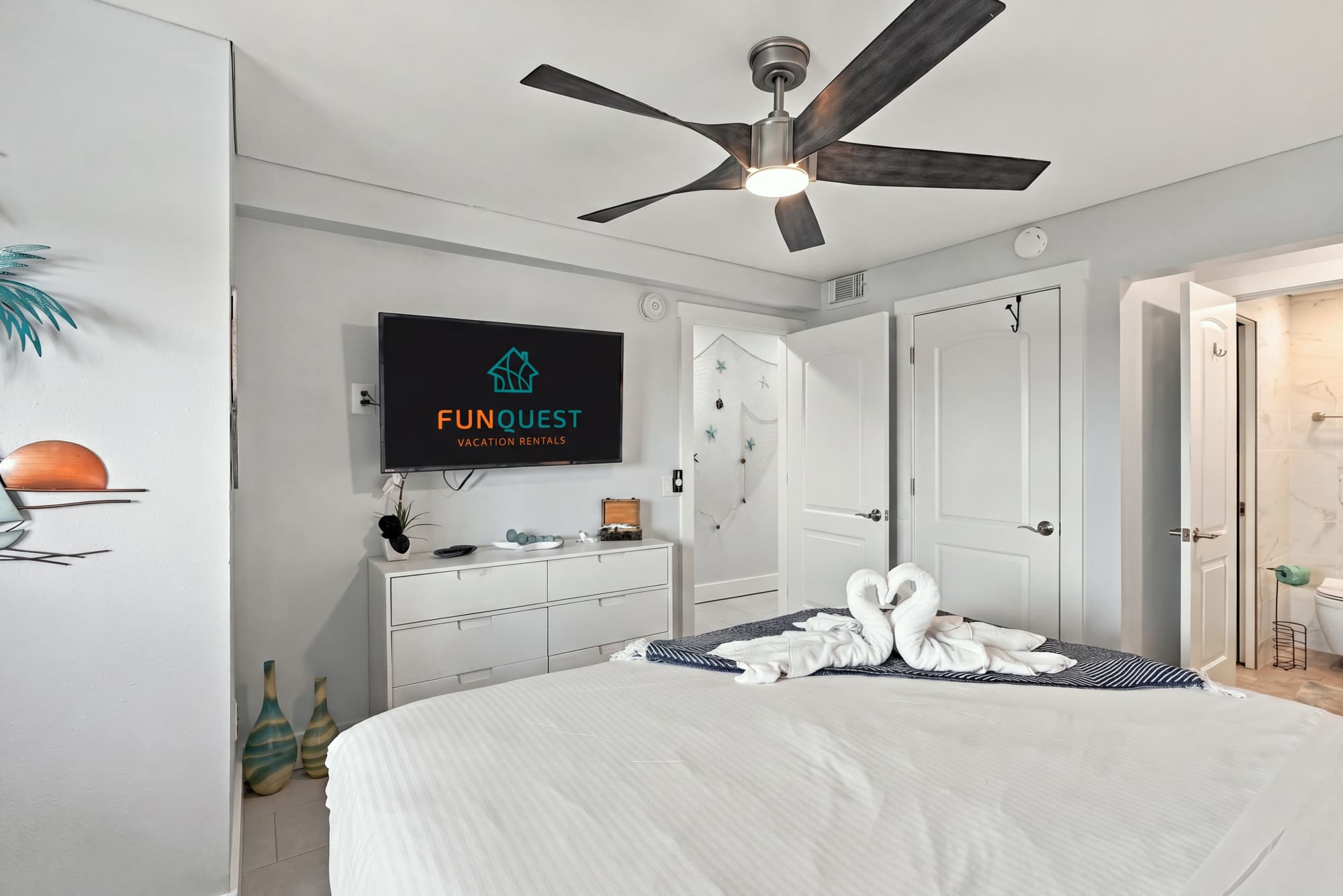 The Summit 1122  – Bedroom with a large bed, wall-mounted TV, ceiling fan, and bathroom door visible.