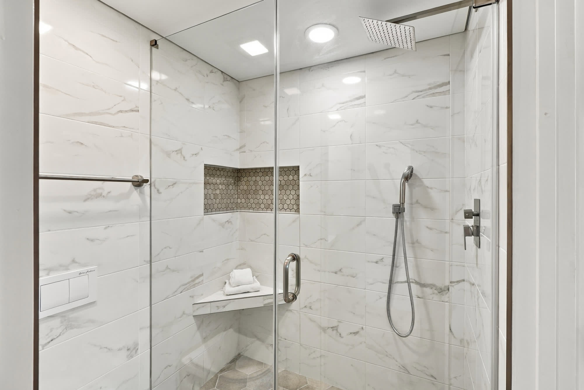 The Summit 1122  – Glass-enclosed shower with marble walls, a built-in shelf, and a hexagonal tile accent.
