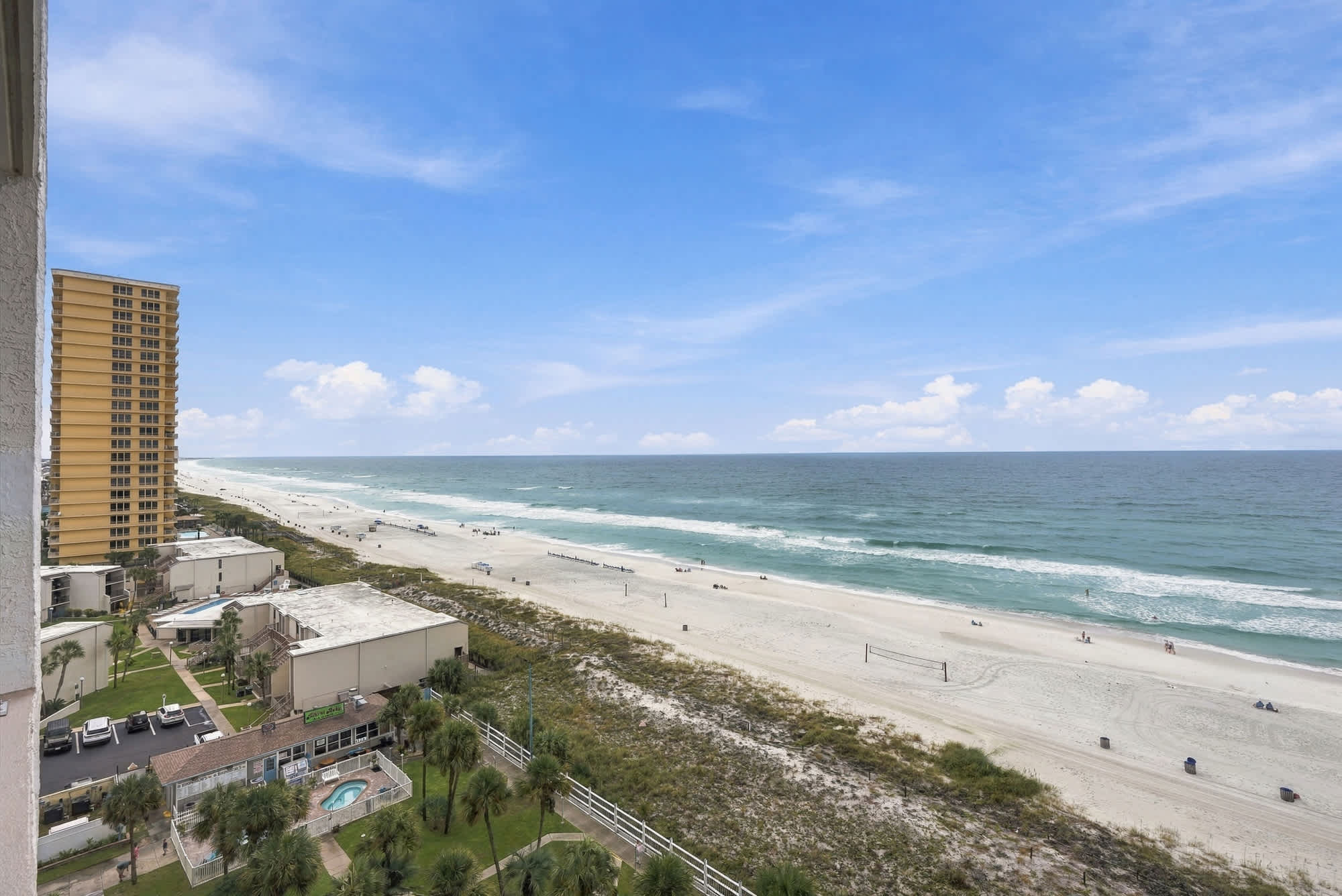 The Summit 1122  – View of the beach with people, ocean waves, and a distant tall building under a clear blue sky.