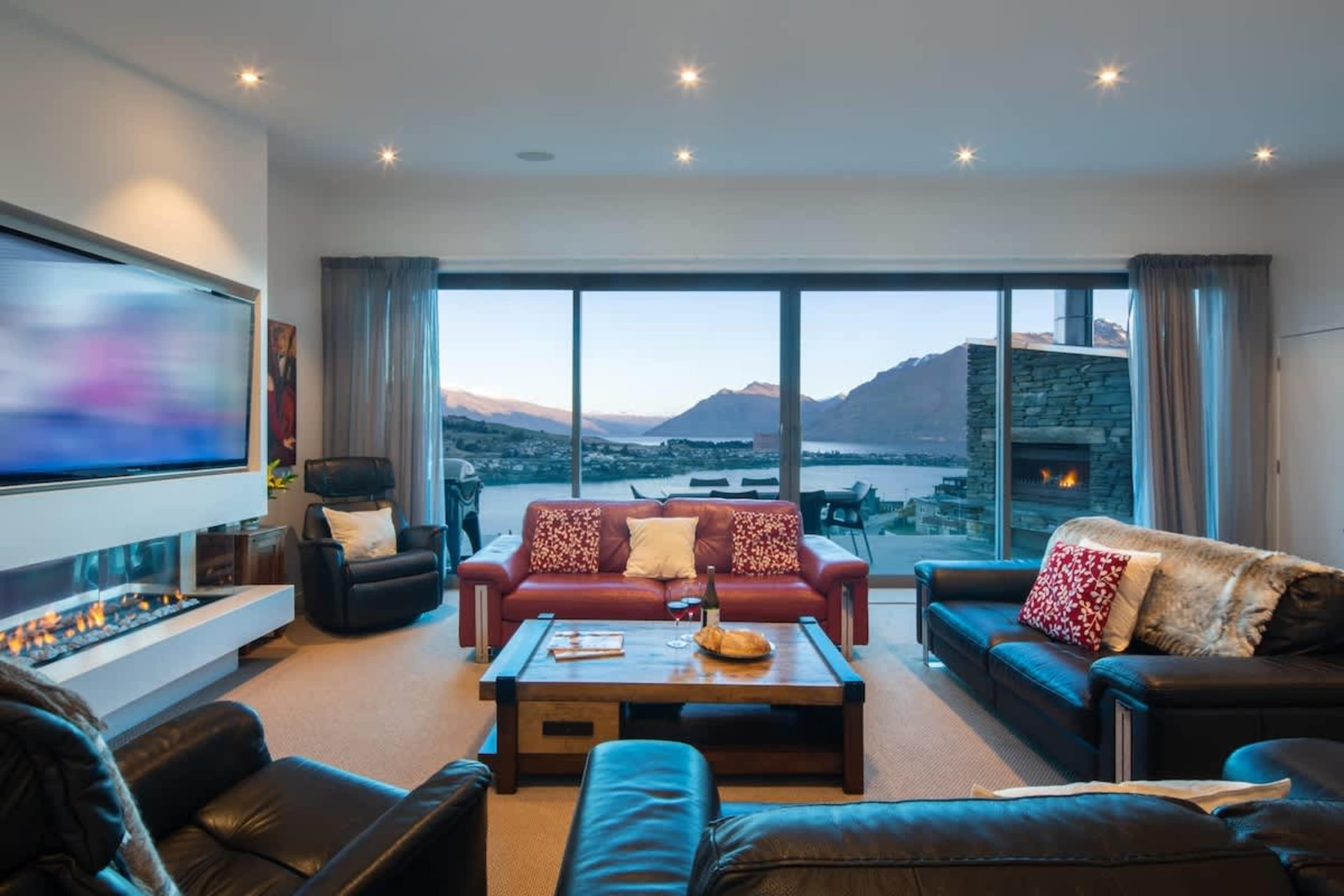 Spacious Living Room with Lake Wakatipu Views – Relax in a bright, sun-filled space featuring floor-to-ceiling windows, stunning panoramas of Lake Wakatipu, and modern, comfortable furnishings.