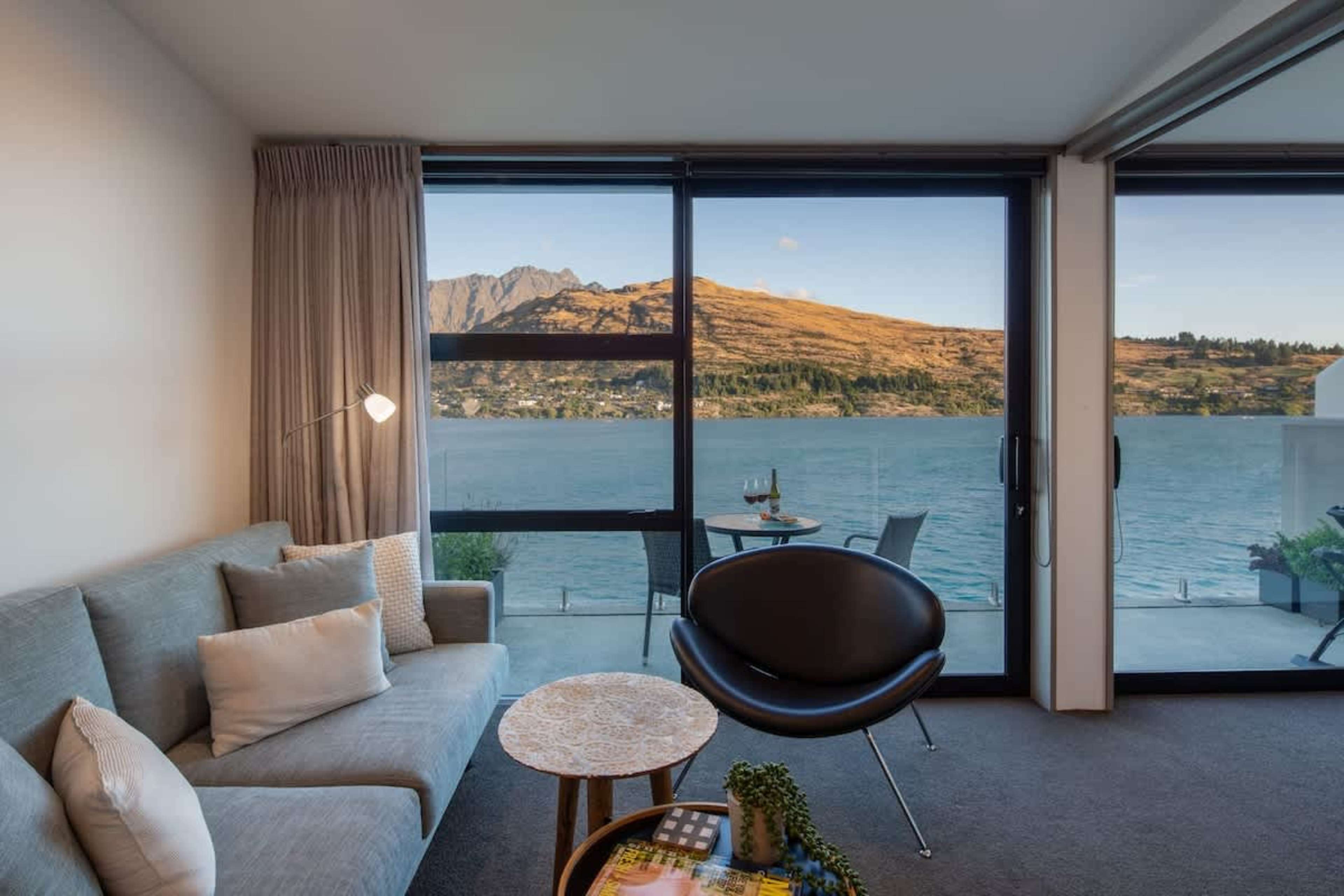 Inviting Living Room with Breathtaking Queenstown Views – Unwind in this cozy living space with floor-to-ceiling windows offering panoramic views of Lake Wakatipu and the Remarkables mountains, a true Queenstown luxury experience.