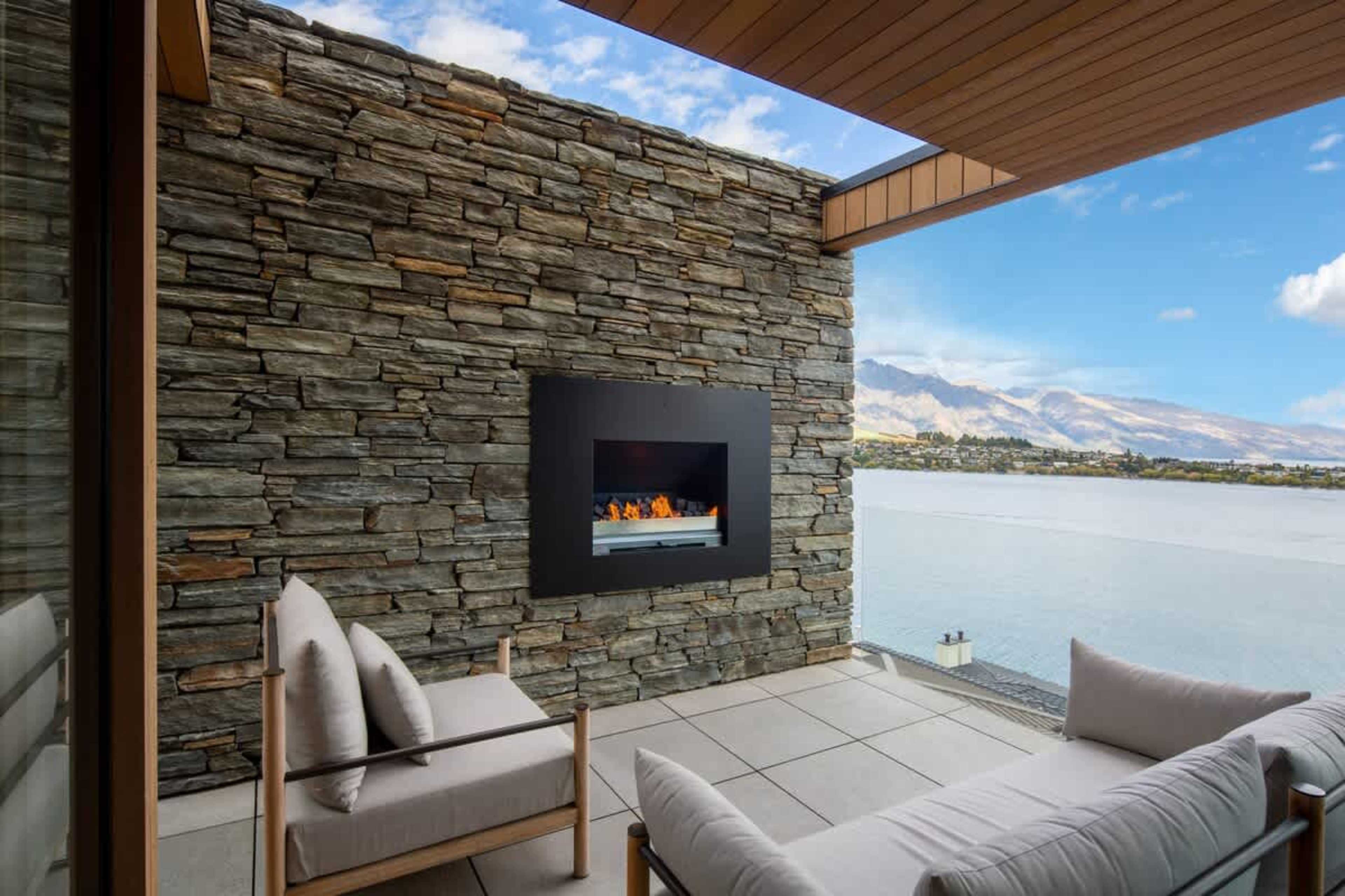 Patio with Fireplace and Stunning Views – Unwind by the outdoor fireplace on the patio, enjoying panoramic views of the lake and mountains, ideal for a peaceful evening of relaxation and natural beauty.
