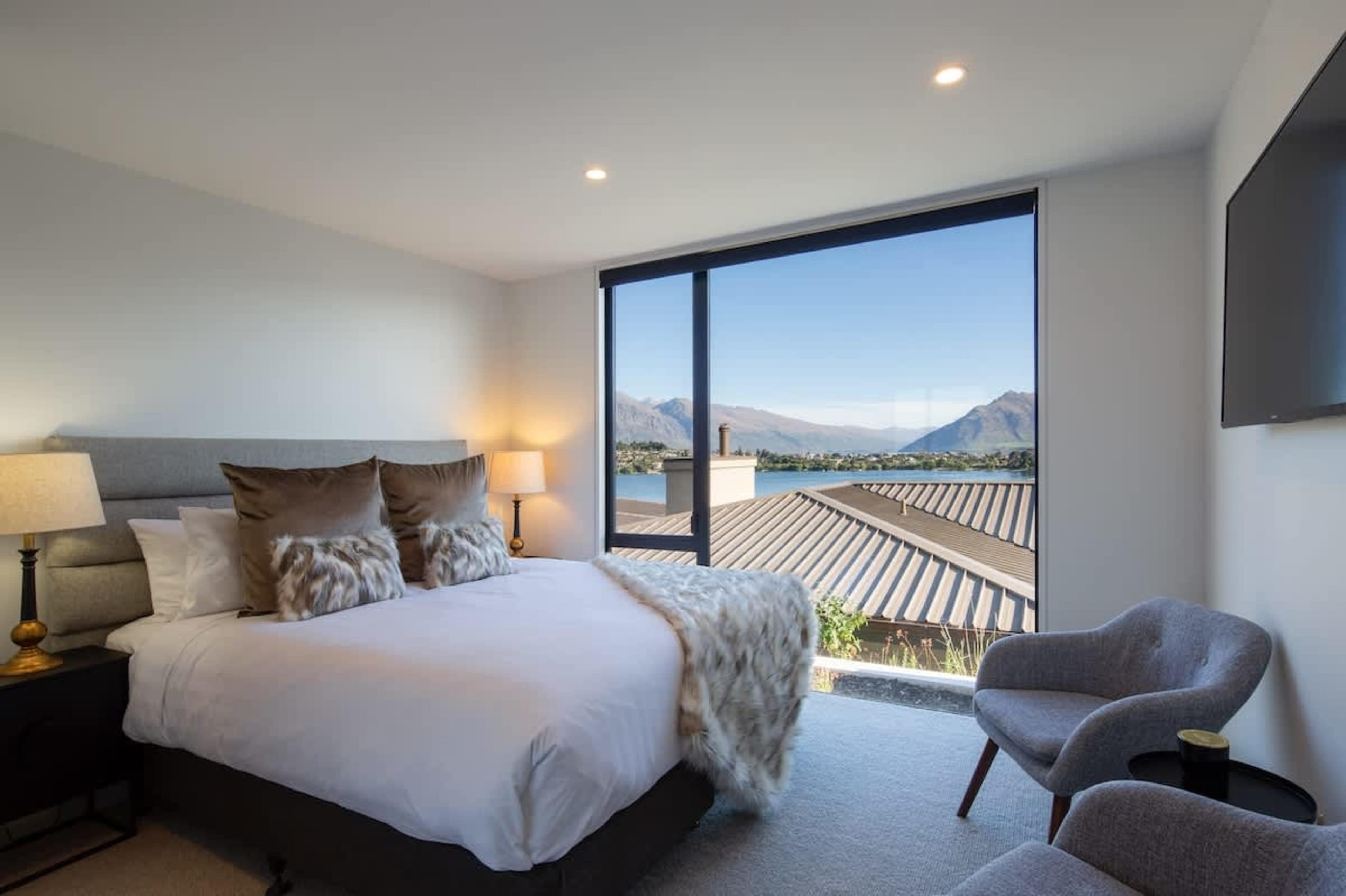This inviting bedroom features a comfortable king-sized bed and large windows that offer breathtaking lake and mountain views. The space is designed for relaxation, with tasteful decor and plenty of natural light, creating a peaceful retreat.