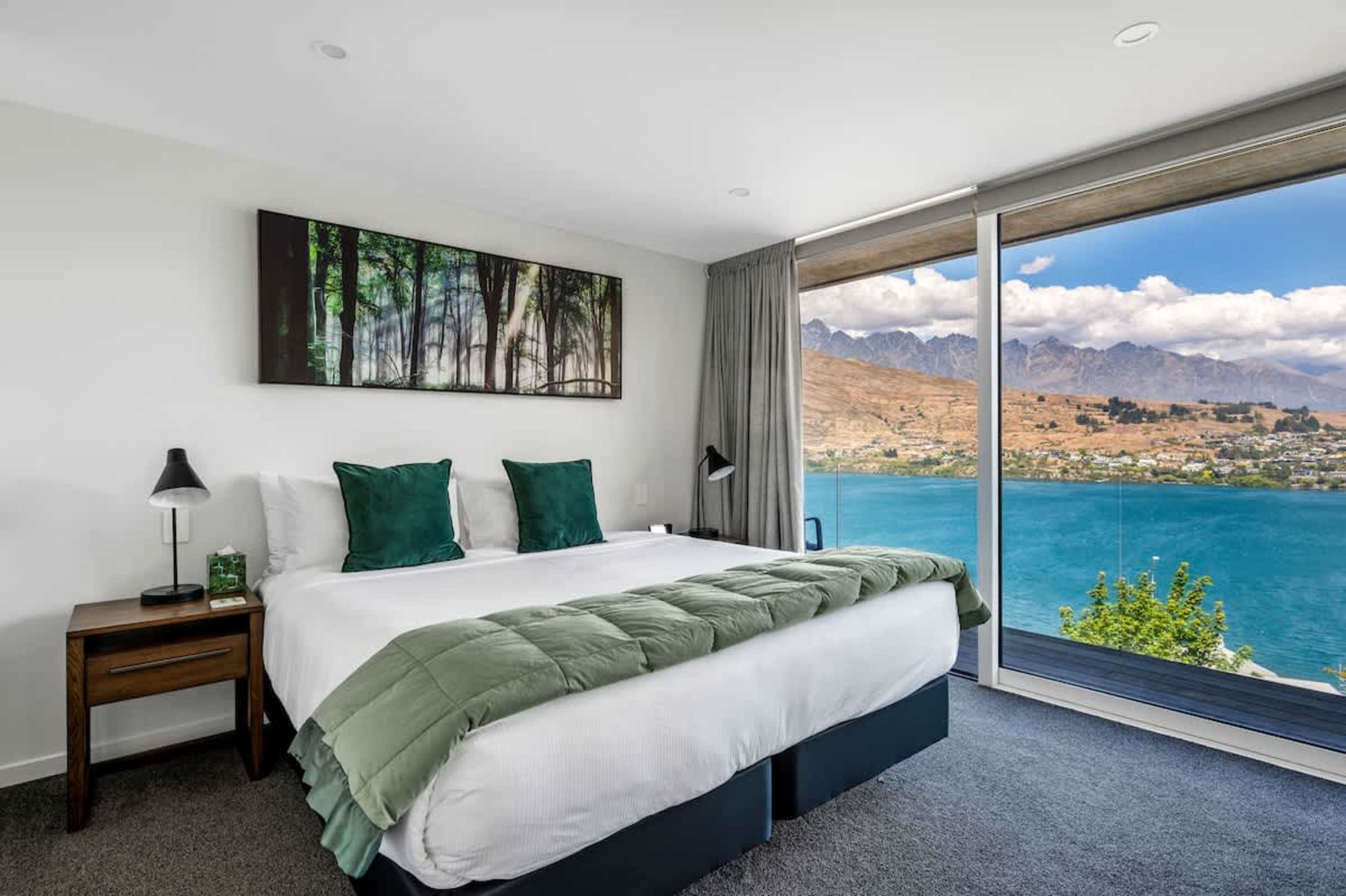 The master bedroom features a king-sized bed, an elegant ensuite with premium finishes, and expansive windows offering stunning views of Lake Wakatipu and the surrounding mountains.