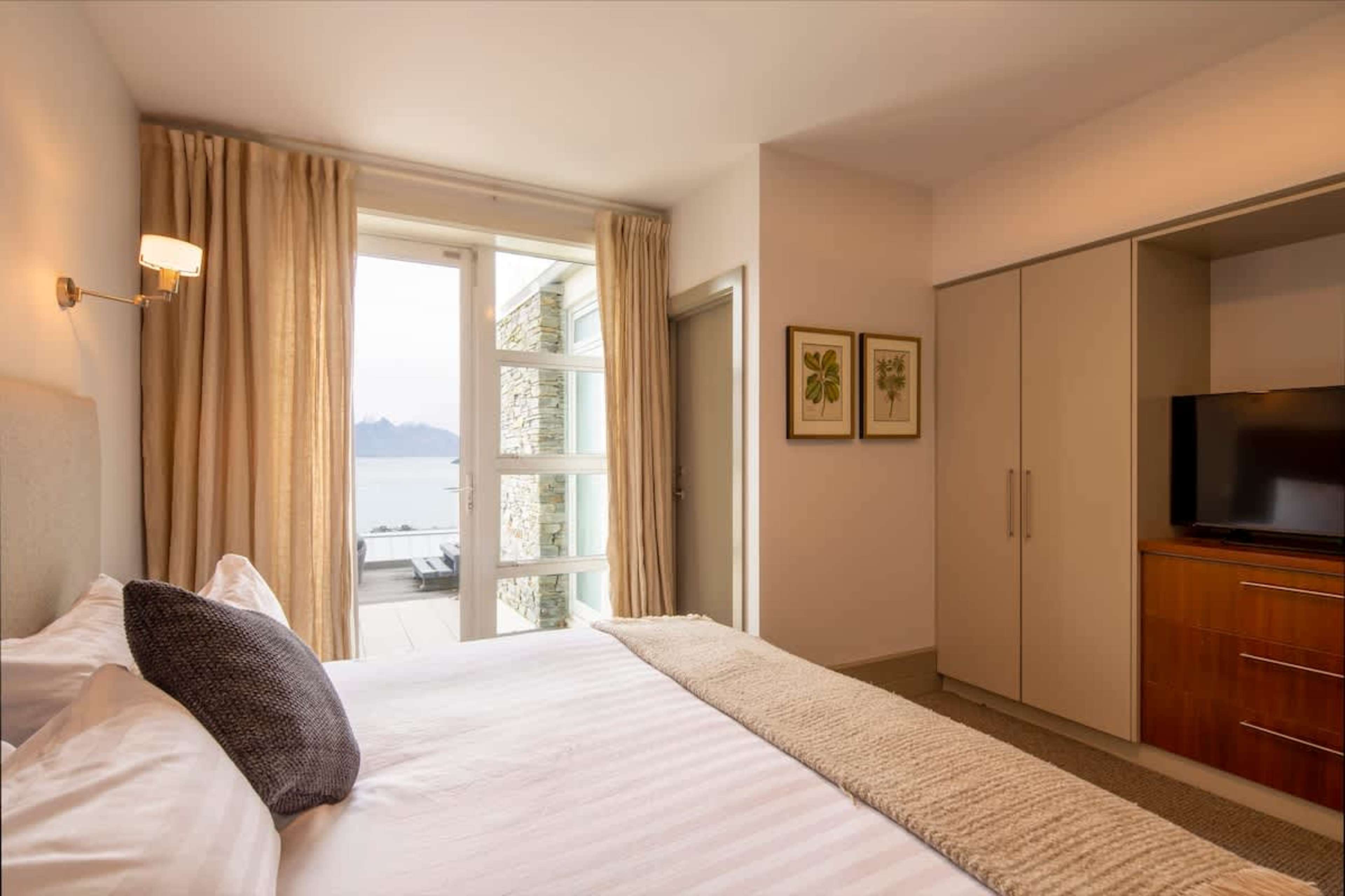 Private Third Bedroom: Enjoy comfort and privacy in this spacious bedroom with an ensuite, direct access to a deck, and stunning lake and mountain views.