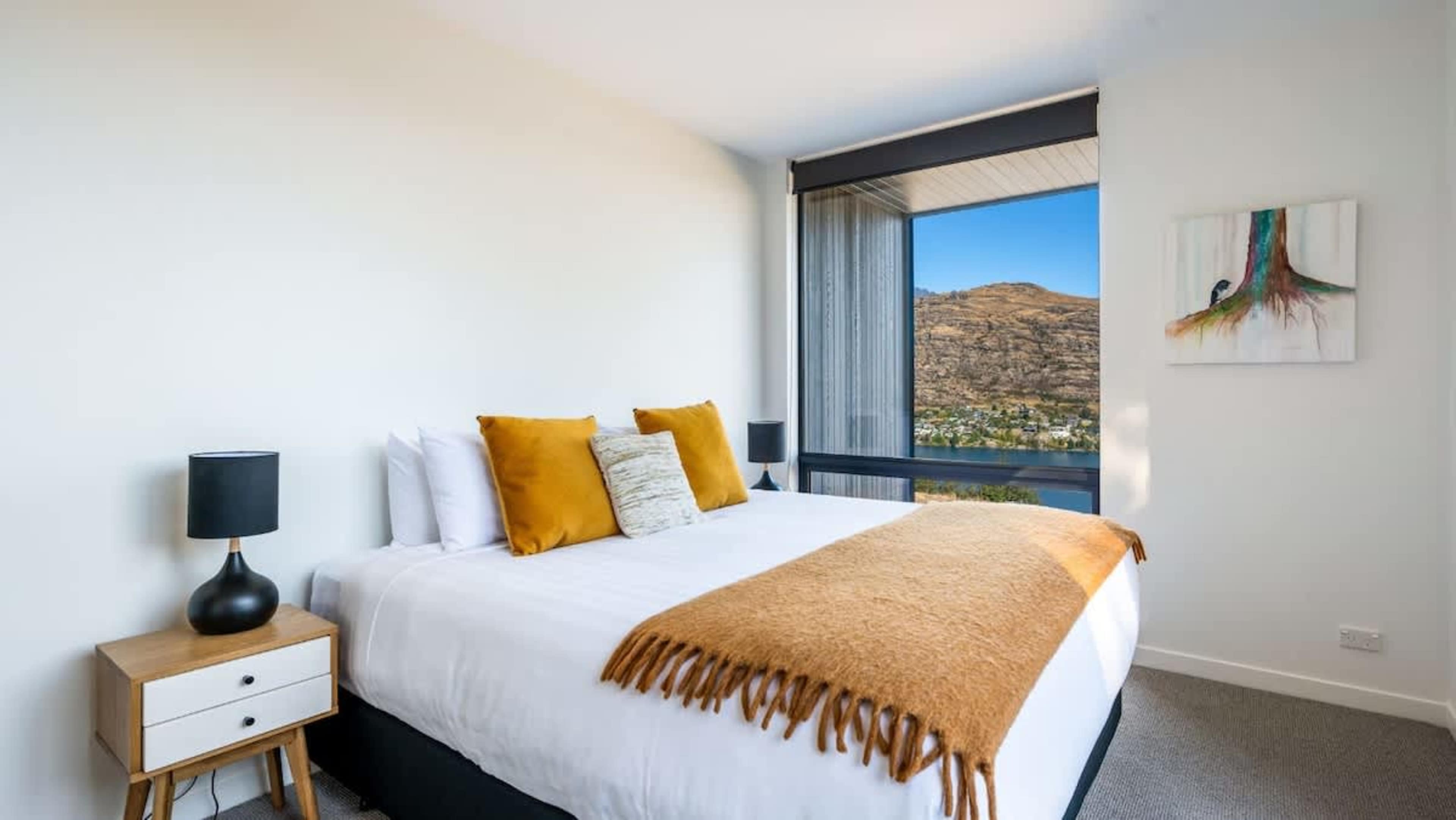 This spacious master bedroom offers a plush king-sized bed, an ensuite with modern fixtures, and a generous wardrobe, all with incredible views of Lake Wakatipu.