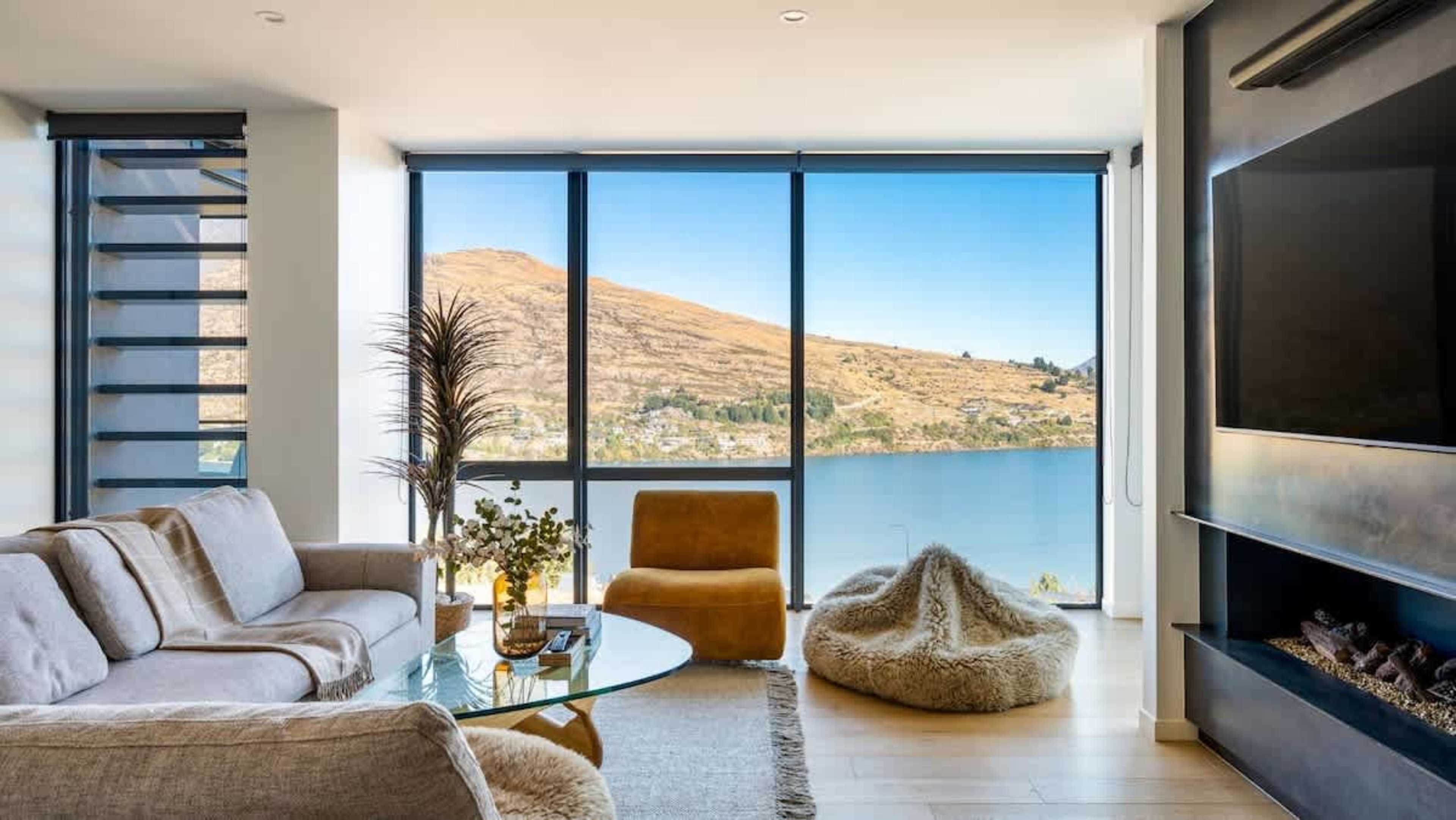 This luxurious living room, part of a brand-new 4-bedroom villa, combines comfort and style with a fireplace, heated floors, and sweeping views of the lake and mountains, making it the perfect retreat.