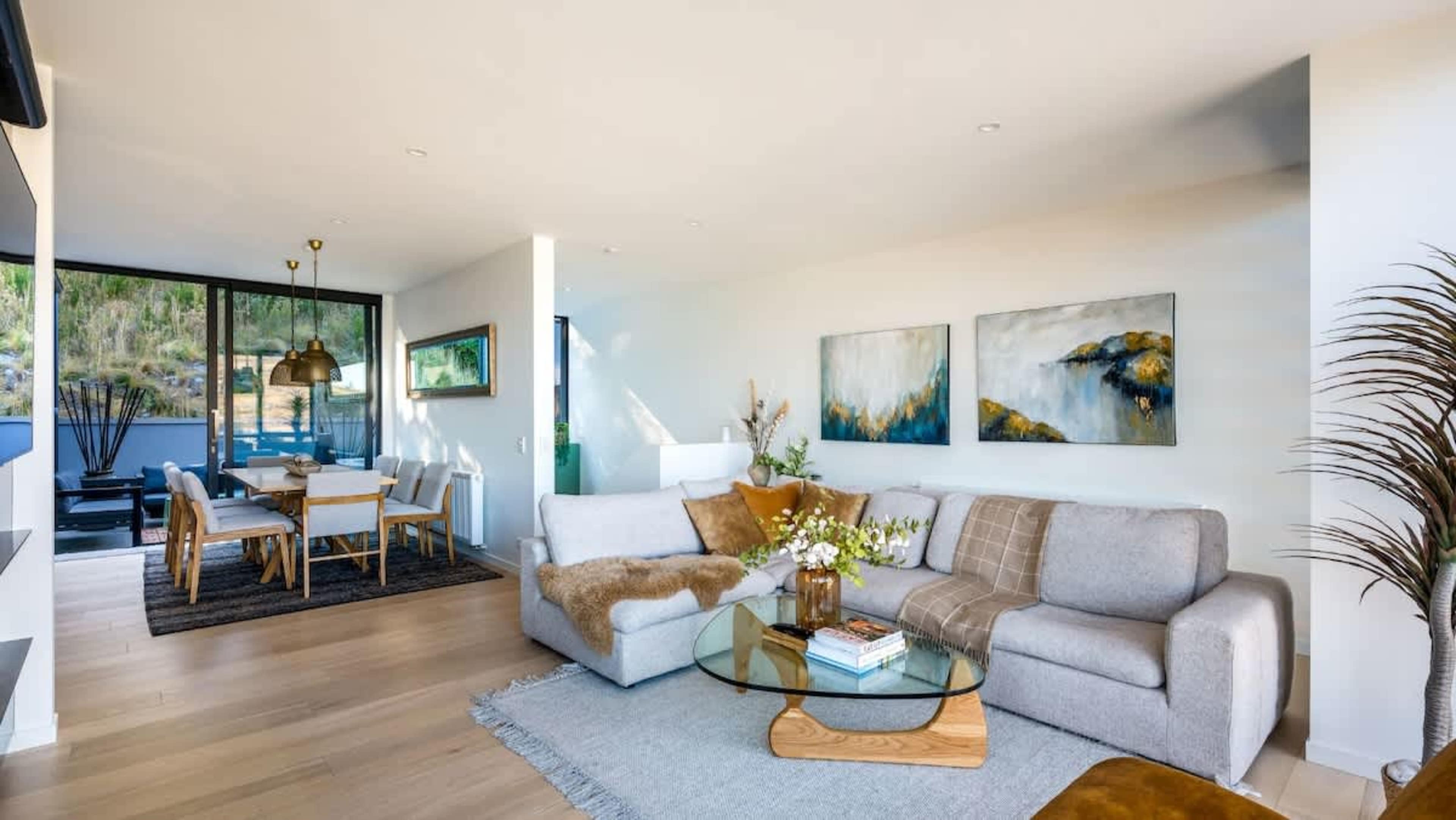 The spacious living room in this brand-new villa offers a luxurious atmosphere with an indoor fireplace, heated floors, and unparalleled views of the surrounding mountains and lake.