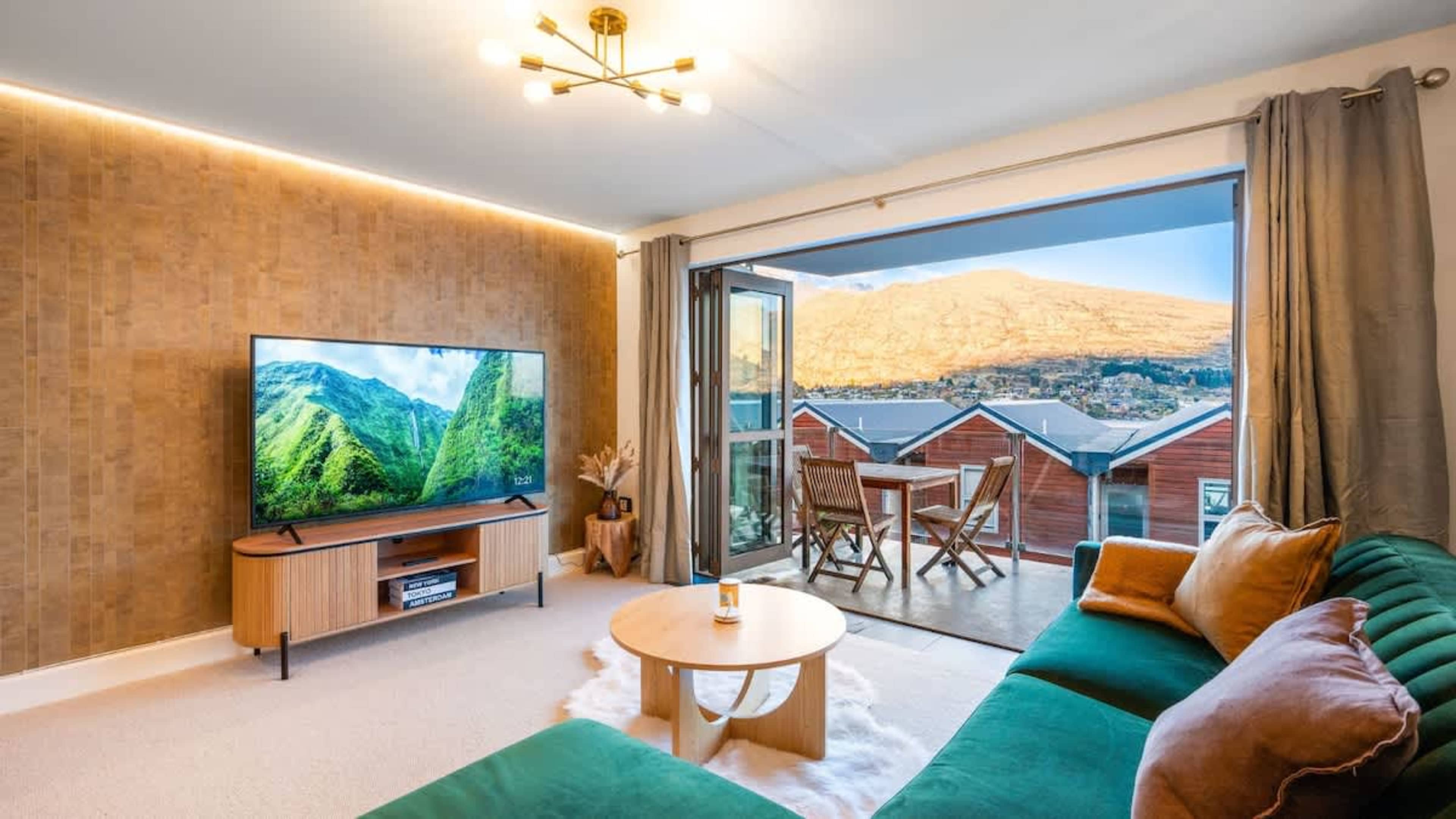 Spacious living room with panoramic lake views, a comfortable sofa, and a smart TV for relaxing evenings in Queenstown.