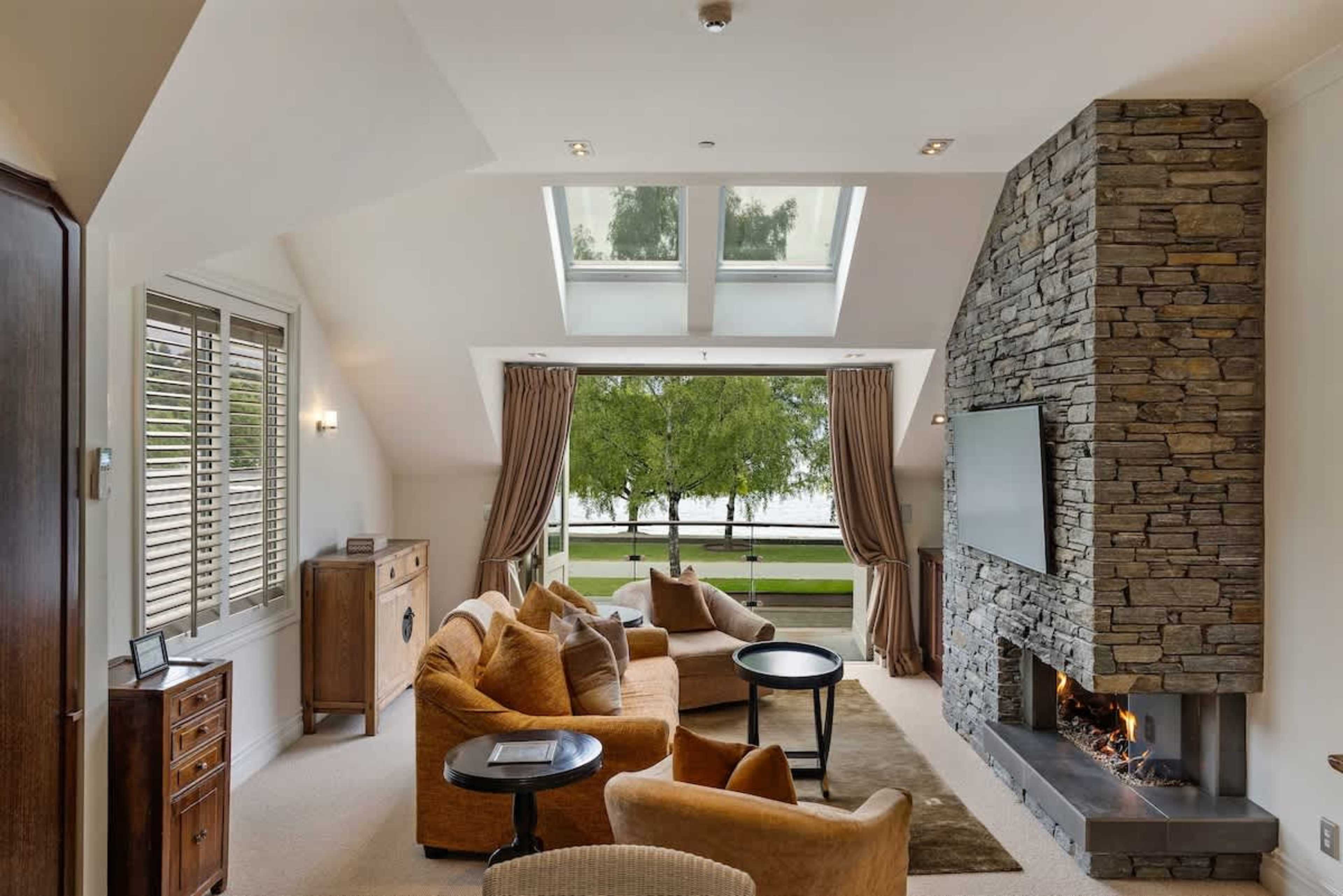 A Queenstown Retreat Like No Other – This stunning living area combines modern elegance with warmth, featuring luxurious furnishings, a gas fire, and a balcony with postcard-perfect views.