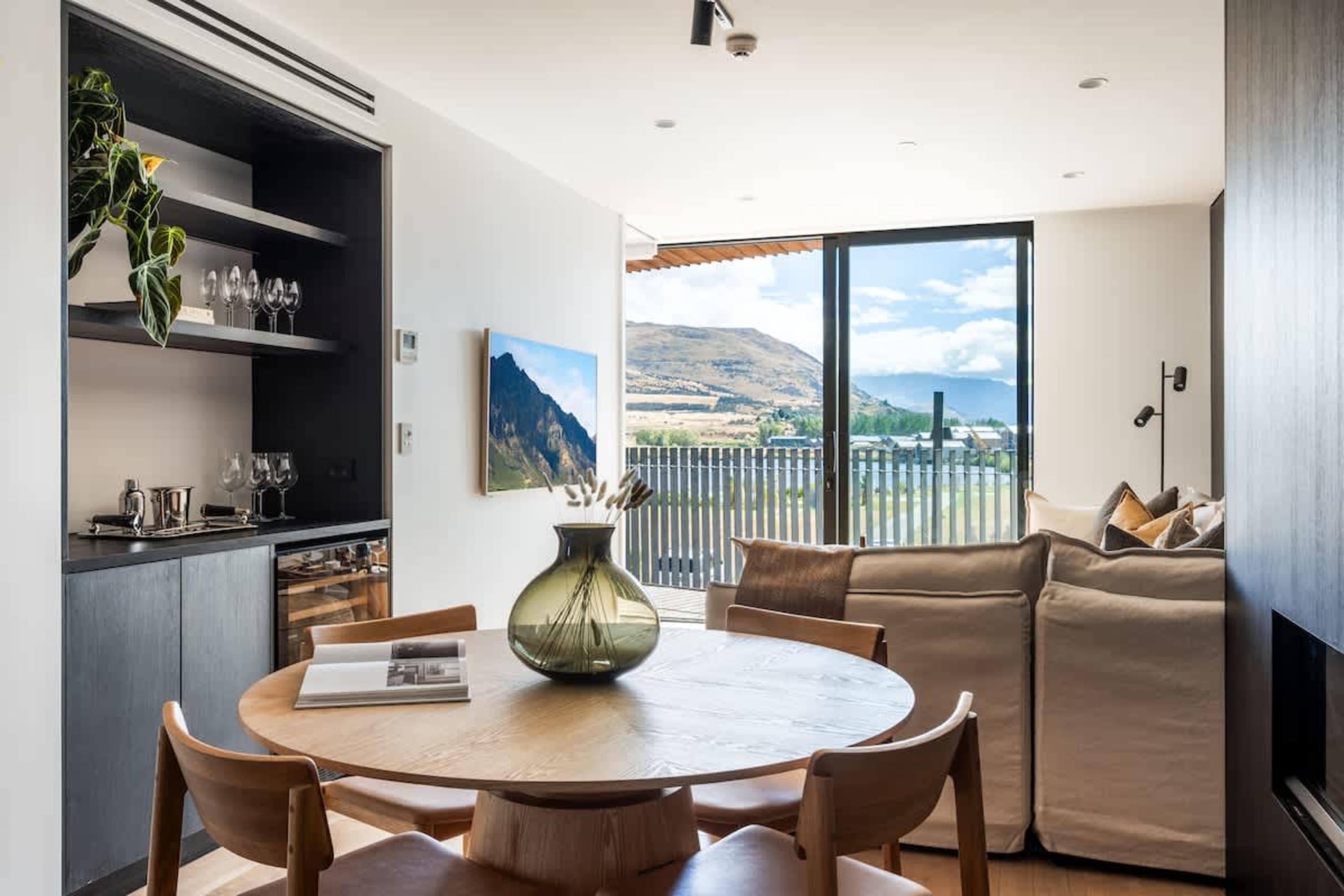 Open-plan dining space at Clubhouse Lane, Jacks Point. Beautiful timber table with mountain lake views, contemporary alpine design, seamlessly connected to kitchen & living. Perfect Queenstown golf course getaway.