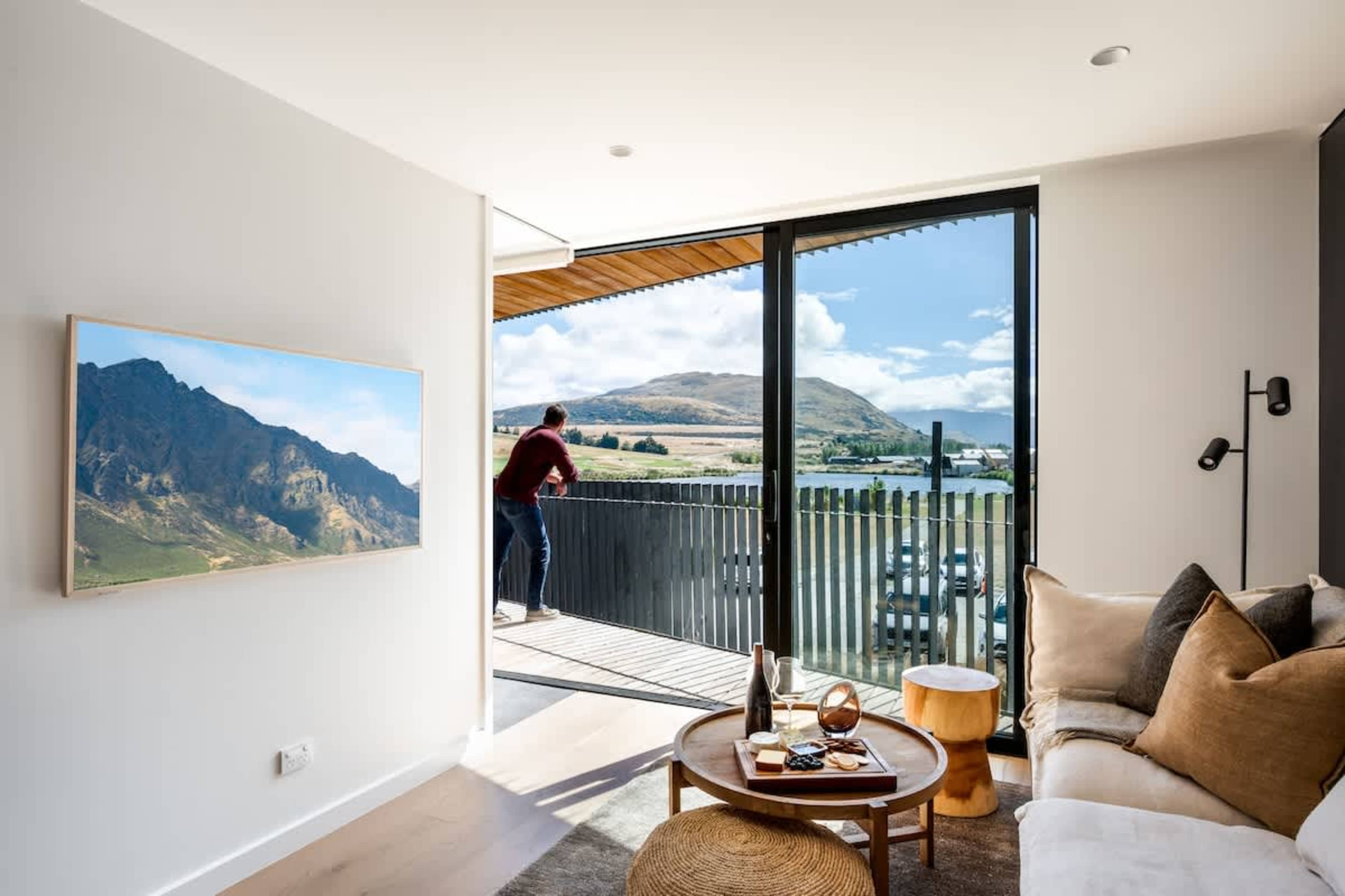 Cozy yet luxurious living room at Clubhouse Lane, Jacks Point Golf Course Queenstown. Panoramic mountain lake views, contemporary alpine design, warm oak floors, high cedar ceilings, fireplace, expansive windows. Ideal golf ski escape.