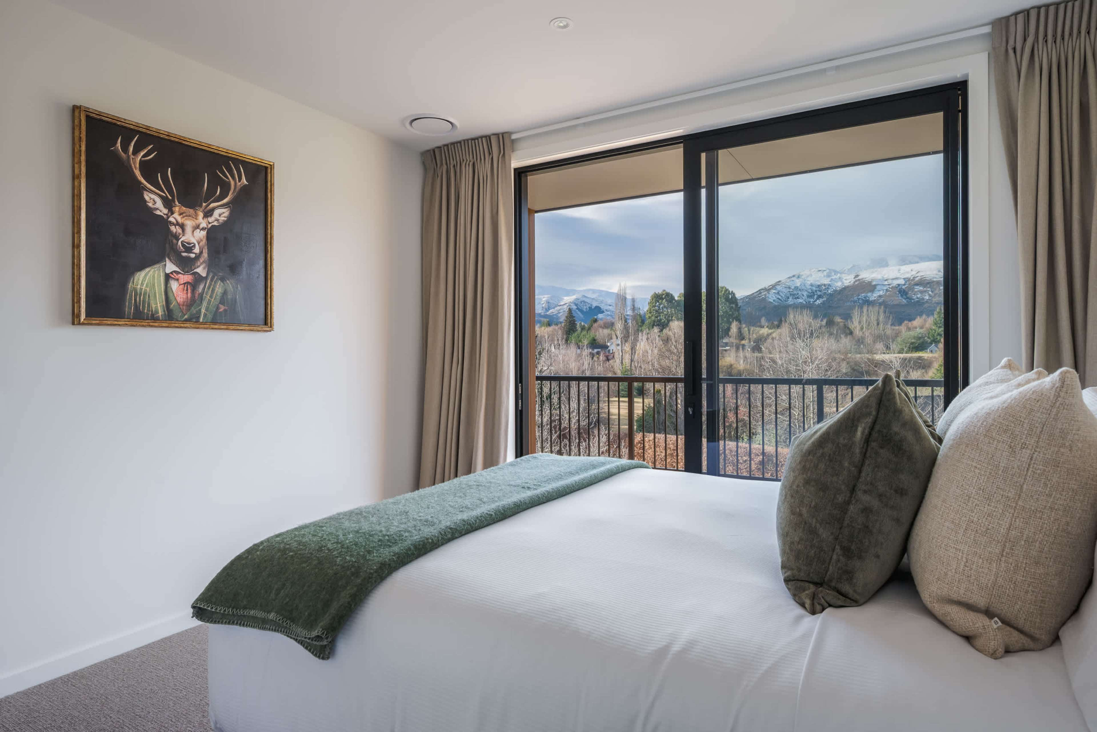 The elegant queen bedroom opens straight onto the deck, where a rugged peak and snow-capped range fill the view under open sky.