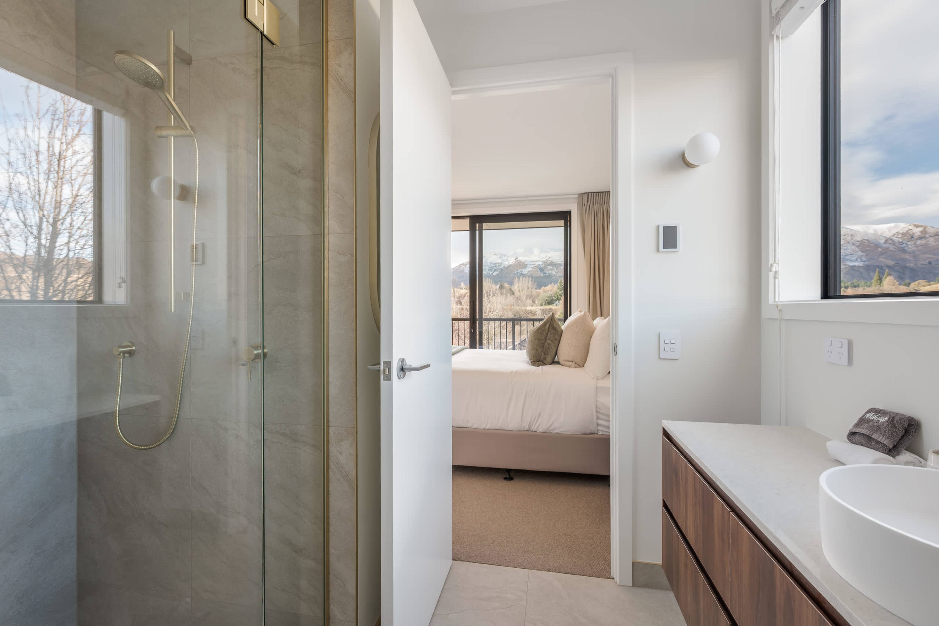 A sleek walk-in shower with brushed gold tapware, and mountain views even from the bathroom.