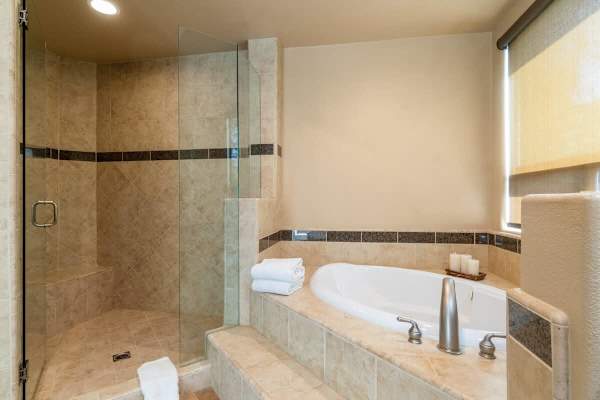 Corner soaking tub and walk-in shower—travertine tile and glass enclosure feel resort-luxurious.