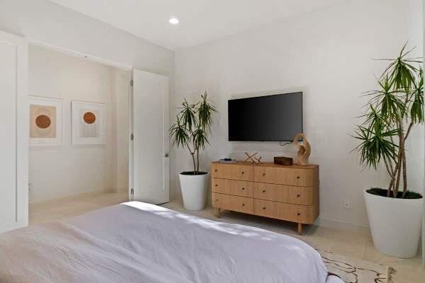 Second bedroom with dual closet doors—crisp white linens and natural wood dresser keep it simple.