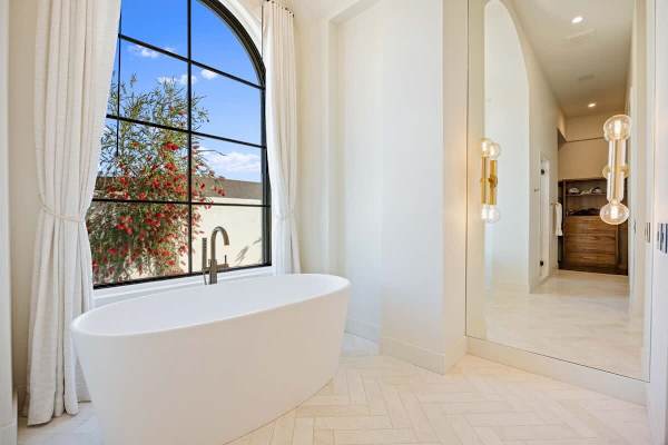Relax in the sculptural tub beneath a dramatic arched black-framed window.