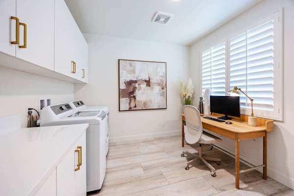 The laundry room doubles as a workspace with a desk, monitor, and reclining office chair.