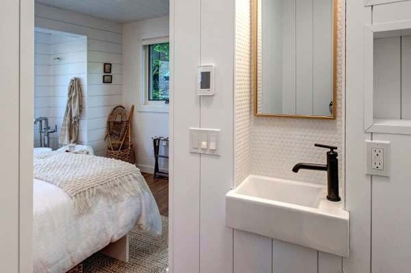 Lofted bedroom in detached guest suite, with a queen bed next to standalone bathtub and half bathroom.
