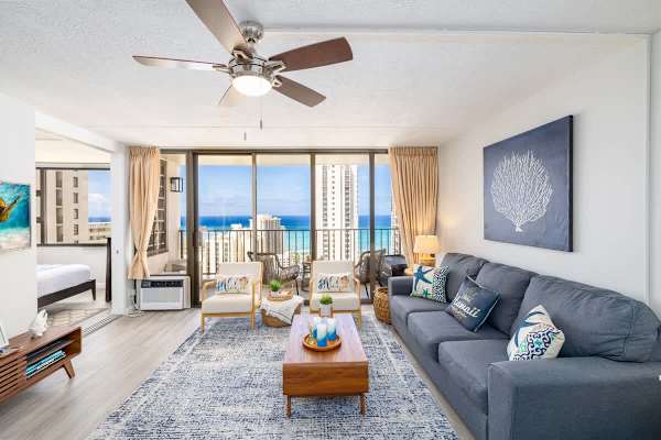 An overview of your living room with a pull-out sleeper sofa, ceiling fan, window AC, and a stunning ocean view.