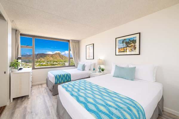 Bright bedroom with two beds and a large window showcasing mountain views.