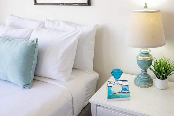 A cozy bedroom corner featuring a white bed with soft pillows and a rustic bedside table with a lamp and decorative accents.