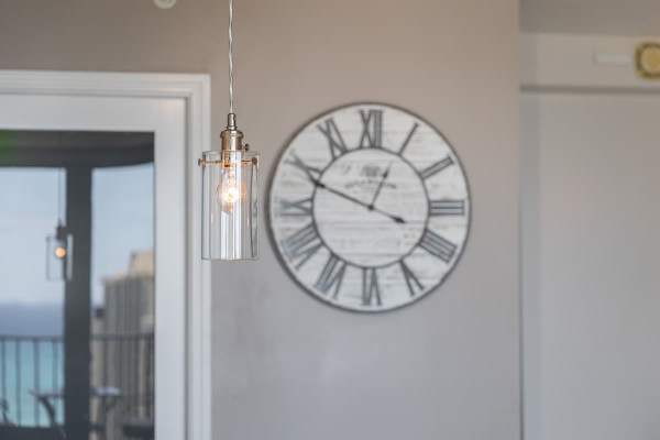 Modern pendant light with a large vintage-style wall clock in the background