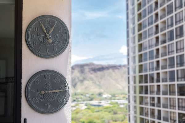 Outdoor wall clock and thermometer with a view of nearby buildings and mountains.