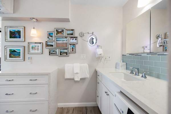Modern bathroom with white cabinetry, blue tile backsplash, and decorative framed photos.