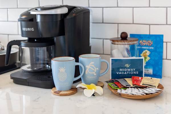 Coffee station with a Keurig machine, two Hawaii-themed mugs, and a selection of coffee and tea packets.