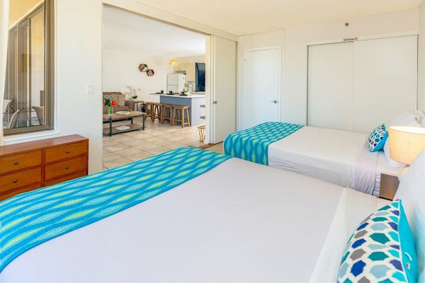 Bright bedroom with two beds and a view into the open living and kitchen area.