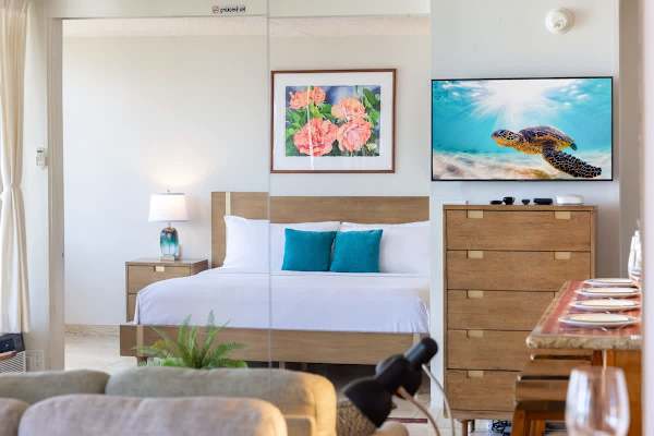 Sunlit bedroom w/ warm wood tones & a welcoming bed styled w/ pops of blue.
