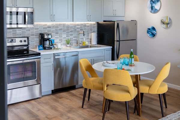 Modern kitchen with stainless steel appliances and a bright dining area featuring yellow chairs.