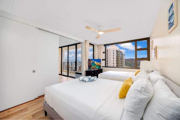 Bright bedroom with two beds and city views through large windows