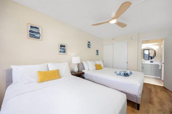 Bright bedroom with two queen beds and modern ceiling fan.