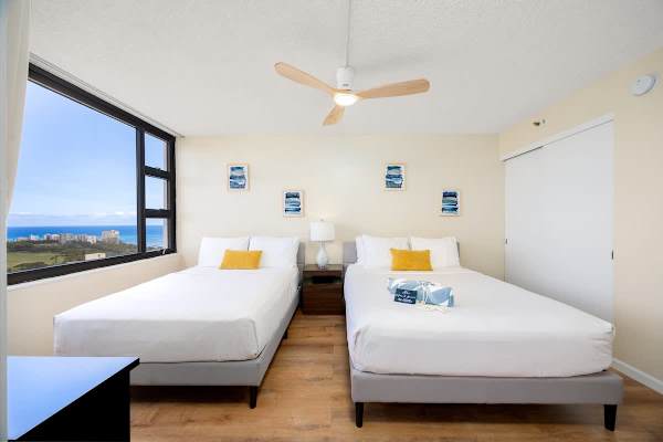 Bright bedroom with two queen beds and ocean views through a large window.
