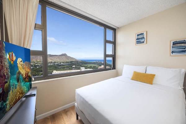 Bright bedroom with a large window offering scenic mountain and ocean views.