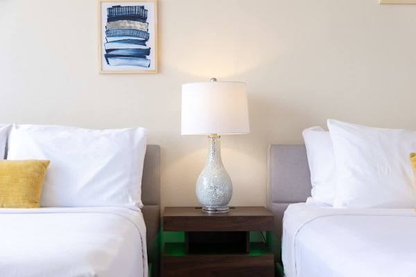 modern bedroom with two beds separated by a wooden nightstand and lamp