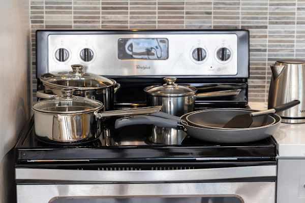 Stainless steel pots and pans arranged on a modern electric stove with a tiled backsplash.