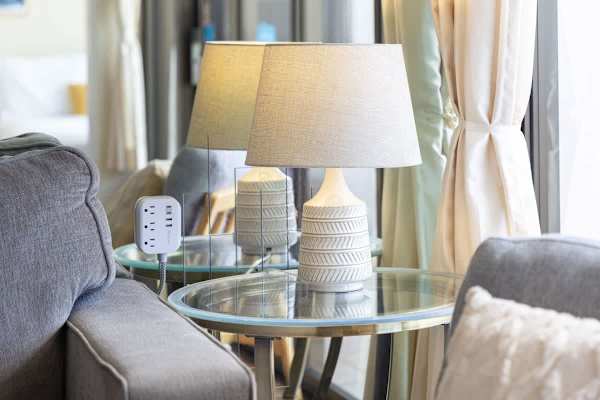 A modern ceramic table lamp on a glass side table next to a comfortable gray sofa.