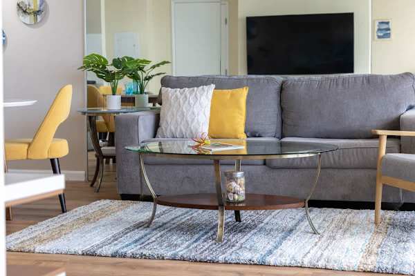 Modern living room with a gray sofa, glass coffee table, and yellow accent chairs for a cozy atmosphere.
