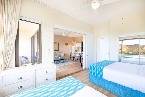 Bright bedroom with twin beds and a view of the living area and balcony.