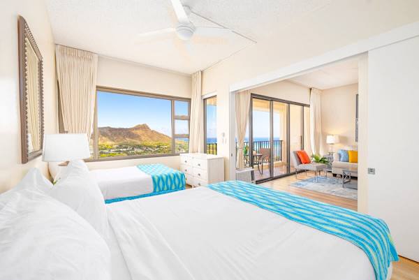 Bright bedroom with ocean and mountain views and access to a balcony seating area.