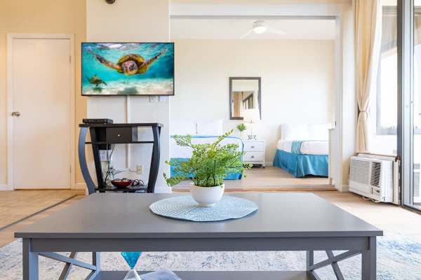 Bright living area with a modern coffee table and a view into the bedroom featuring twin beds.
